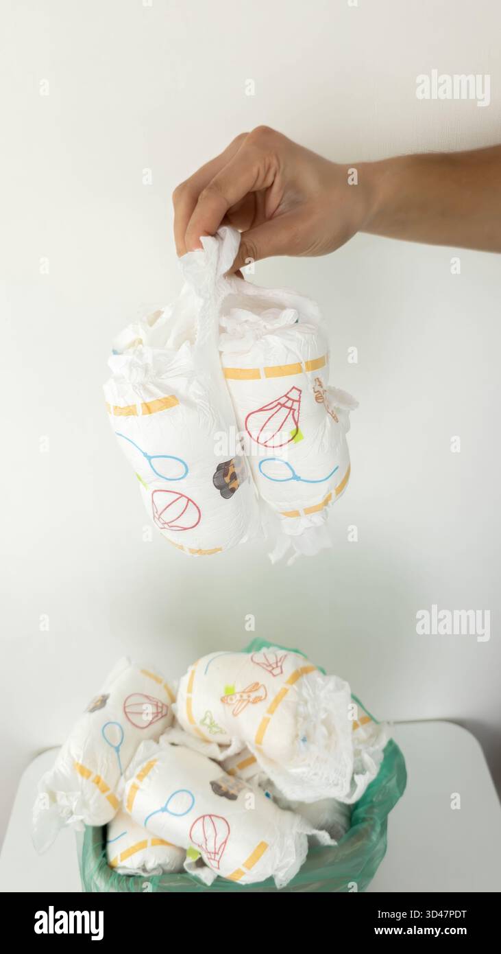 Die Hand wirft gebrauchte Windeln in den vollen Papierkorb. Stockfoto