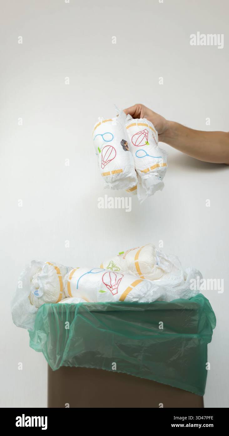 Die Hand wirft gebrauchte Windeln in den vollen Papierkorb. Stockfoto