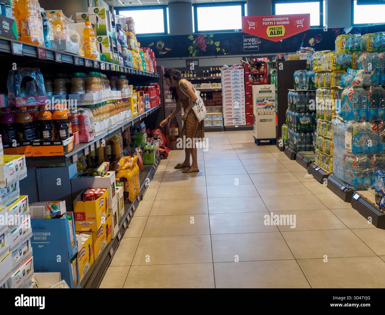 Cremona, Italien 11. August 2025 weibliche Käuferin, die Getränke in Flaschen entlang des Kühlgangs im Budget-Supermarkt auswählt, Saft und Wa scannt Stockfoto
