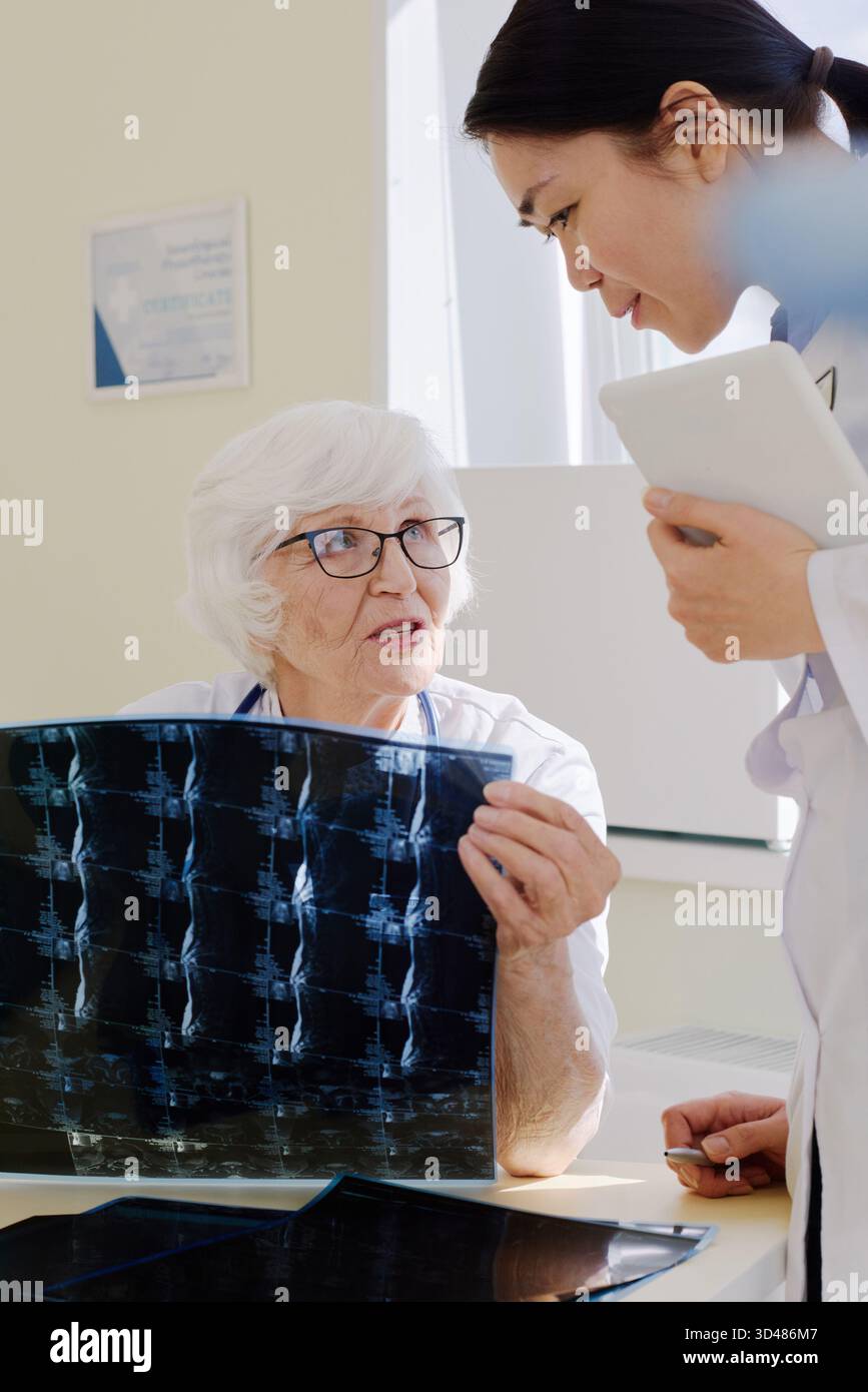 Reife Arztpraxis mit junger Assistentin bei der Röntgenuntersuchung des Patienten nach MRT-Verfahren im Krankenhaus Stockfoto