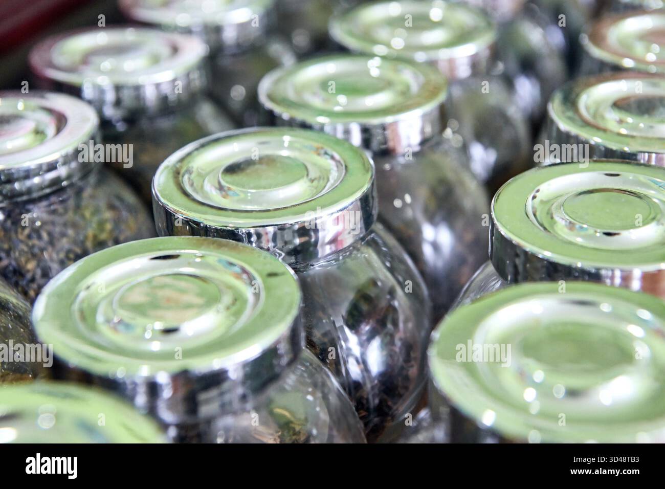 Nahaufnahme von Glasgläsern mit Metalldeckeln gefüllt mit verschiedenen getrockneten Tees in einer Ladenanzeige. Stockfoto