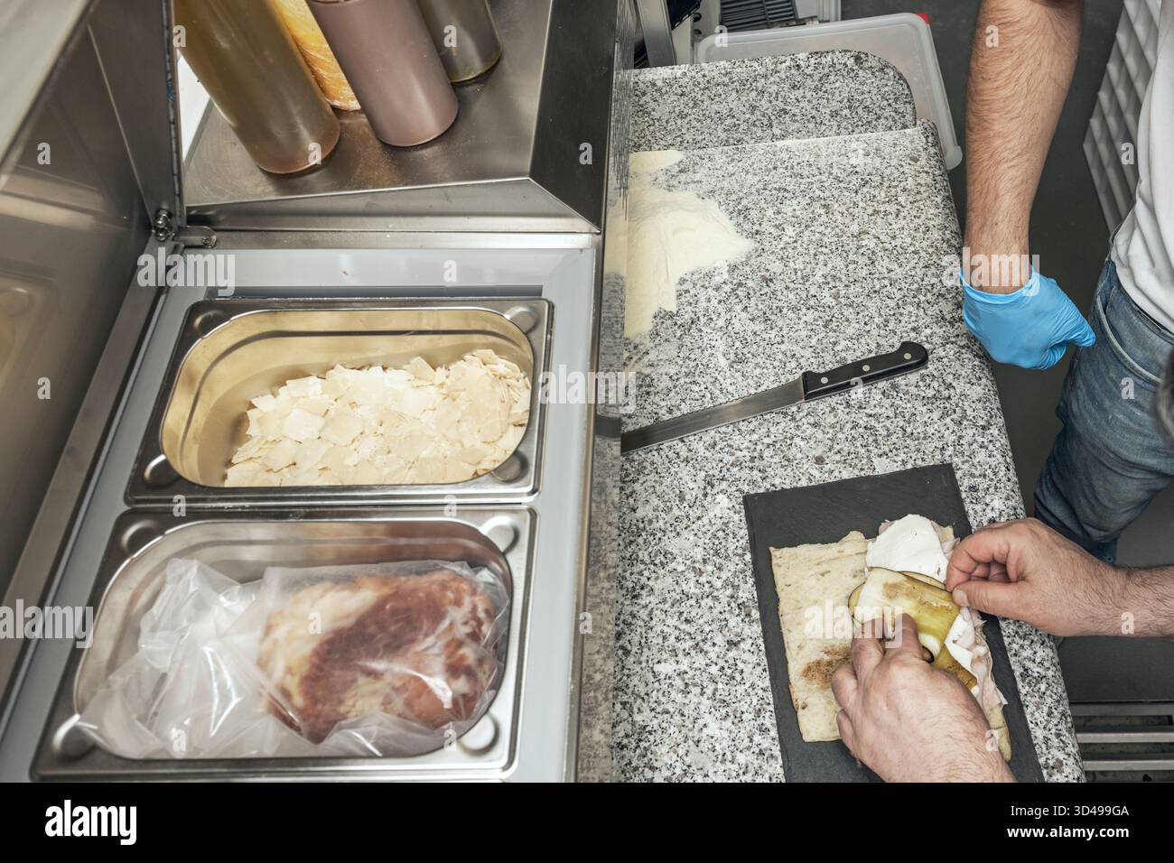 Unter gleichmäßigem Druck von Fachhänden gleitet ein Holzstift über den Focaccia-Teig und verteilt ihn auf dem bemehlten Granit. Stockfoto