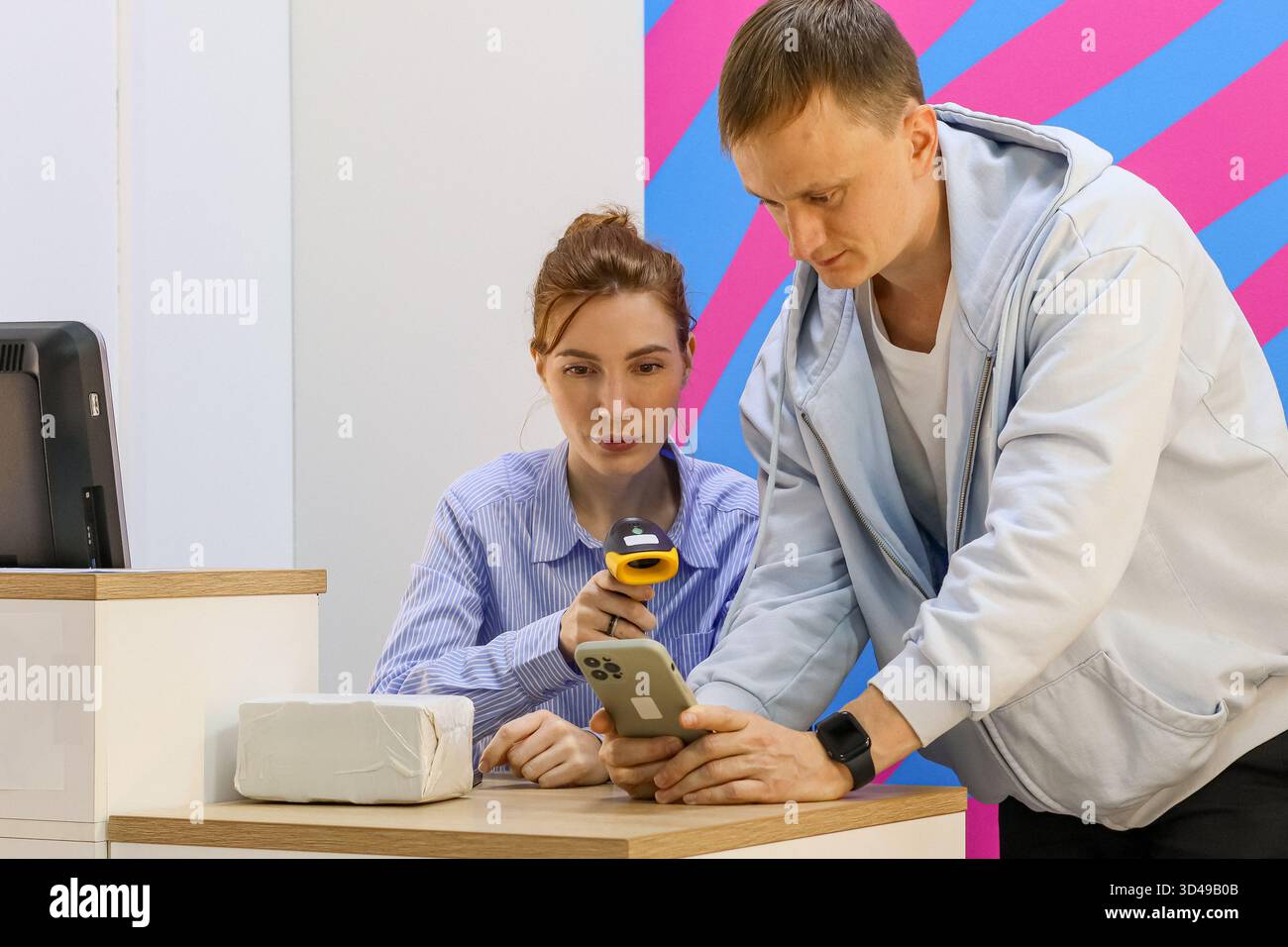 Mitarbeiter scannt das Telefon des Kunden am Abholschalter mit dem Paket auf dem Tisch. Stockfoto