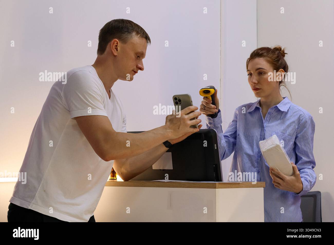 Kunde zeigt dem Mitarbeiter das Smartphone, das es am Abholschalter scannt. Mann in weißem Hemd hält Telefon, während Frau in blauem Hemd Scanner darauf benutzt Stockfoto