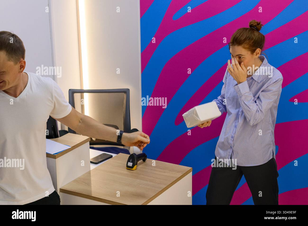 Mann scannt das Paket, während die Frau es hält und die Nase bedeckt. Stockfoto