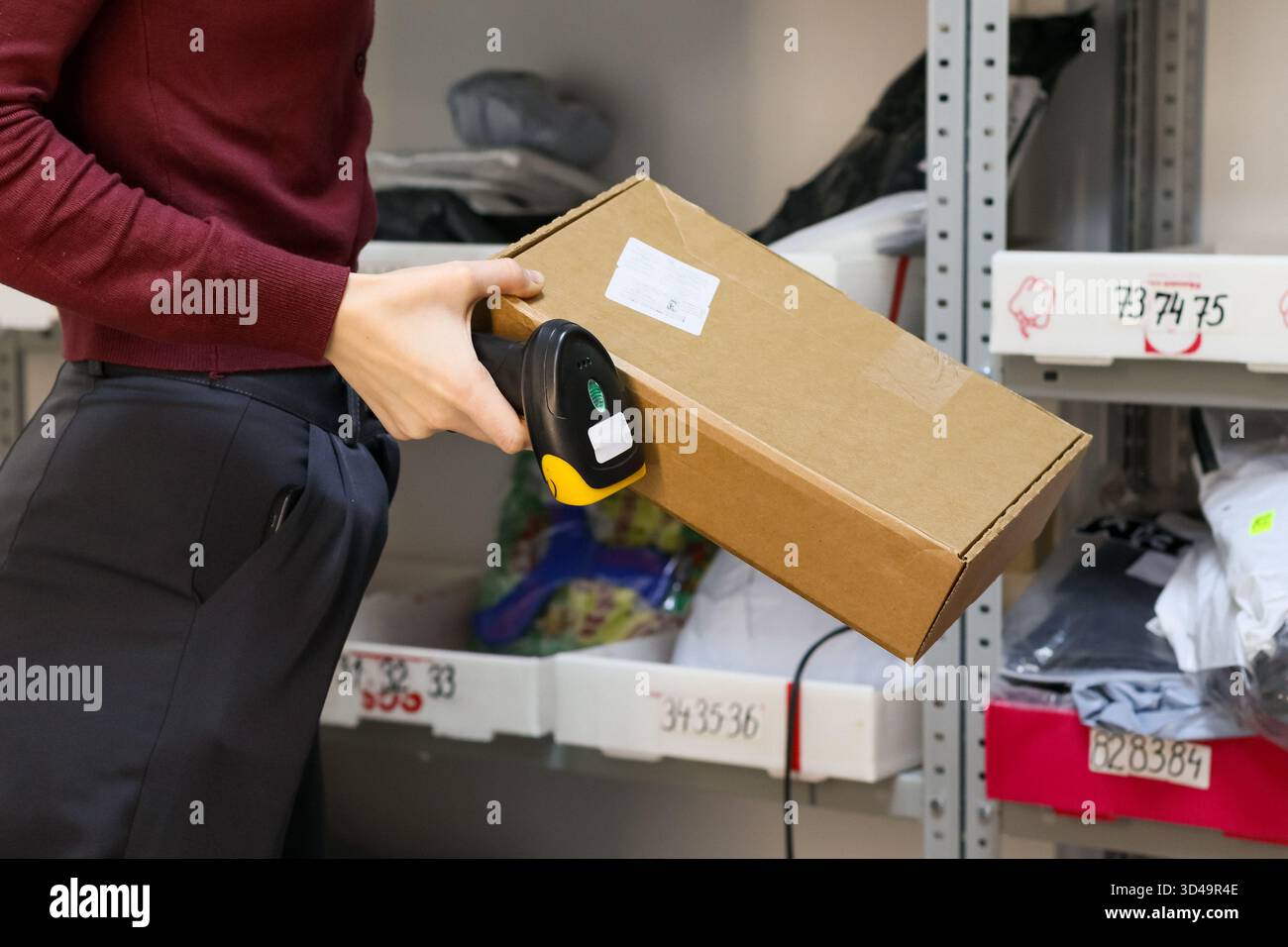 Mitarbeiter scannt Paketbarcode im Lagerbereich. Nahaufnahme des Handlesers an braunem Kartonetikett auf dem Regal mit verschiedenen Paketen Stockfoto