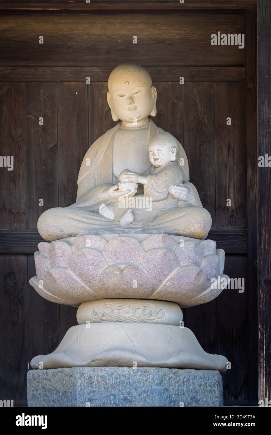 Skulptur von Maitreya Buddha mit kleinen Bdudha und Urne betend in Lotusposition in Obuse, Japan Stockfoto