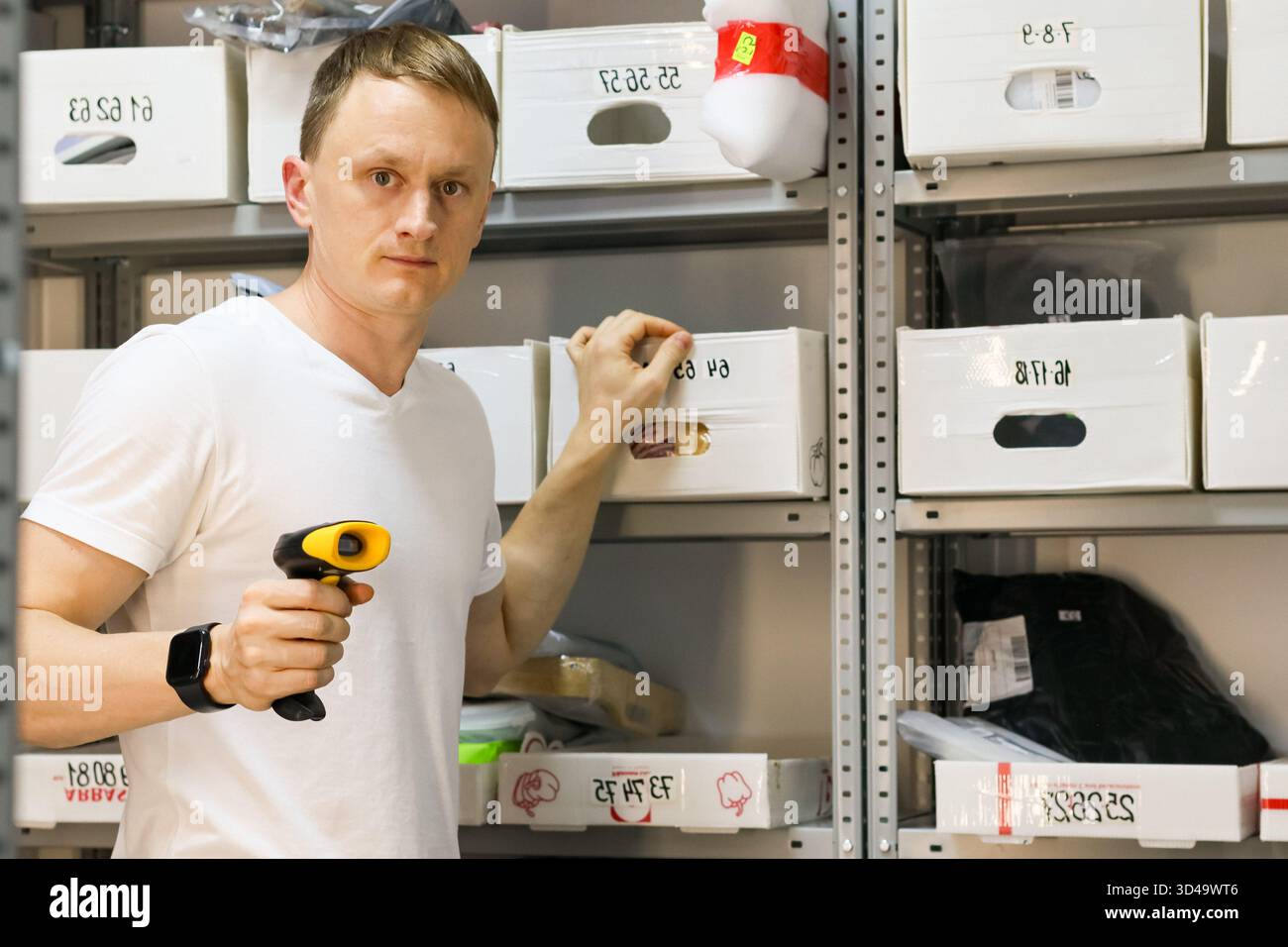 Etikett des Mitarbeiters im Lagerregal. Männlicher Arbeiter, der den Scanner an den Containercode im Regal hält, um das Abhollager zu bestellen Stockfoto