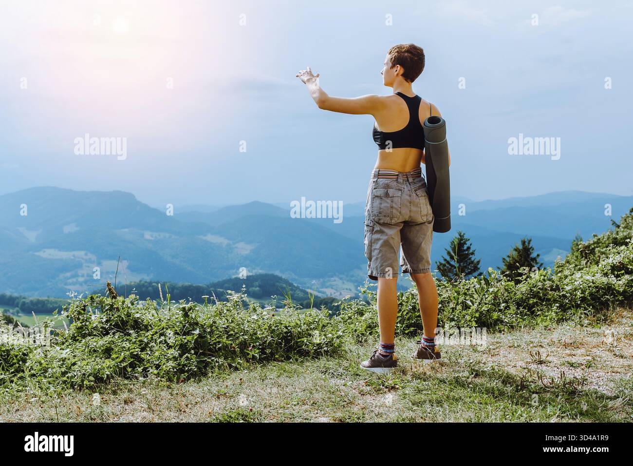 Attraktiver, sportlicher Blick von hinten auf die Berge, während sie auf hohen Felsen stehen Stockfoto