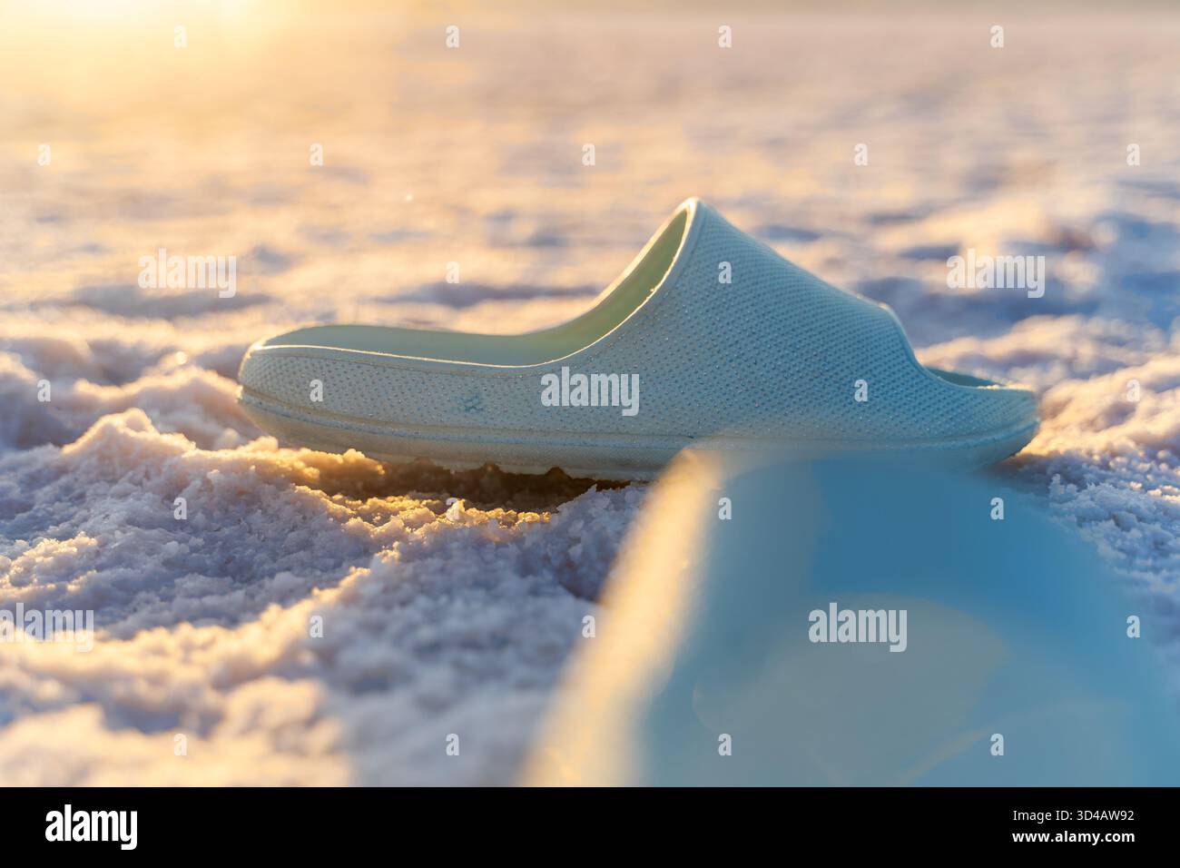 Ein blauer Slipper liegt auf einer kristallklaren Salzoberfläche, beleuchtet von warmem, goldenem Abendsonnenlicht. Stockfoto
