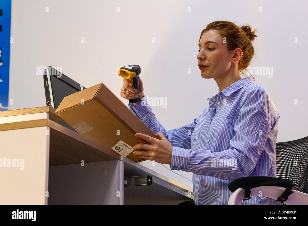 Mitarbeiter scannt Barcode auf dem Paket an der Zustellstation. Seitenansicht der Hebebox für weibliche Mitarbeiter und des Zielscanners auf das Etikett im Arbeitsbereich Stockfoto