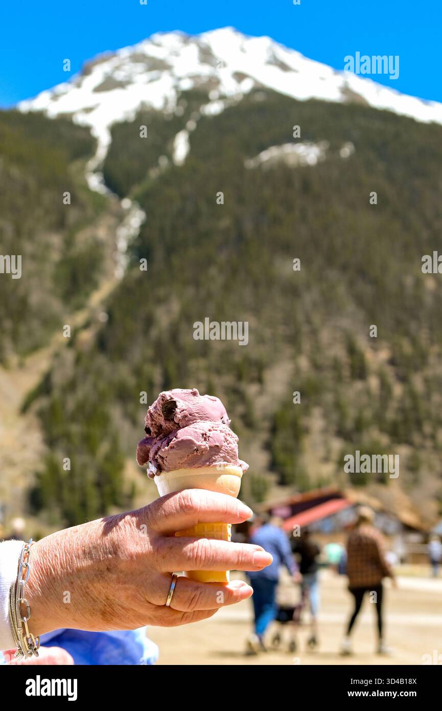 Nahaufnahme einer Person im Urlaub mit einem Kegel mit Kirscheis und einem schneebedeckten Berg im Hintergrund Stockfoto