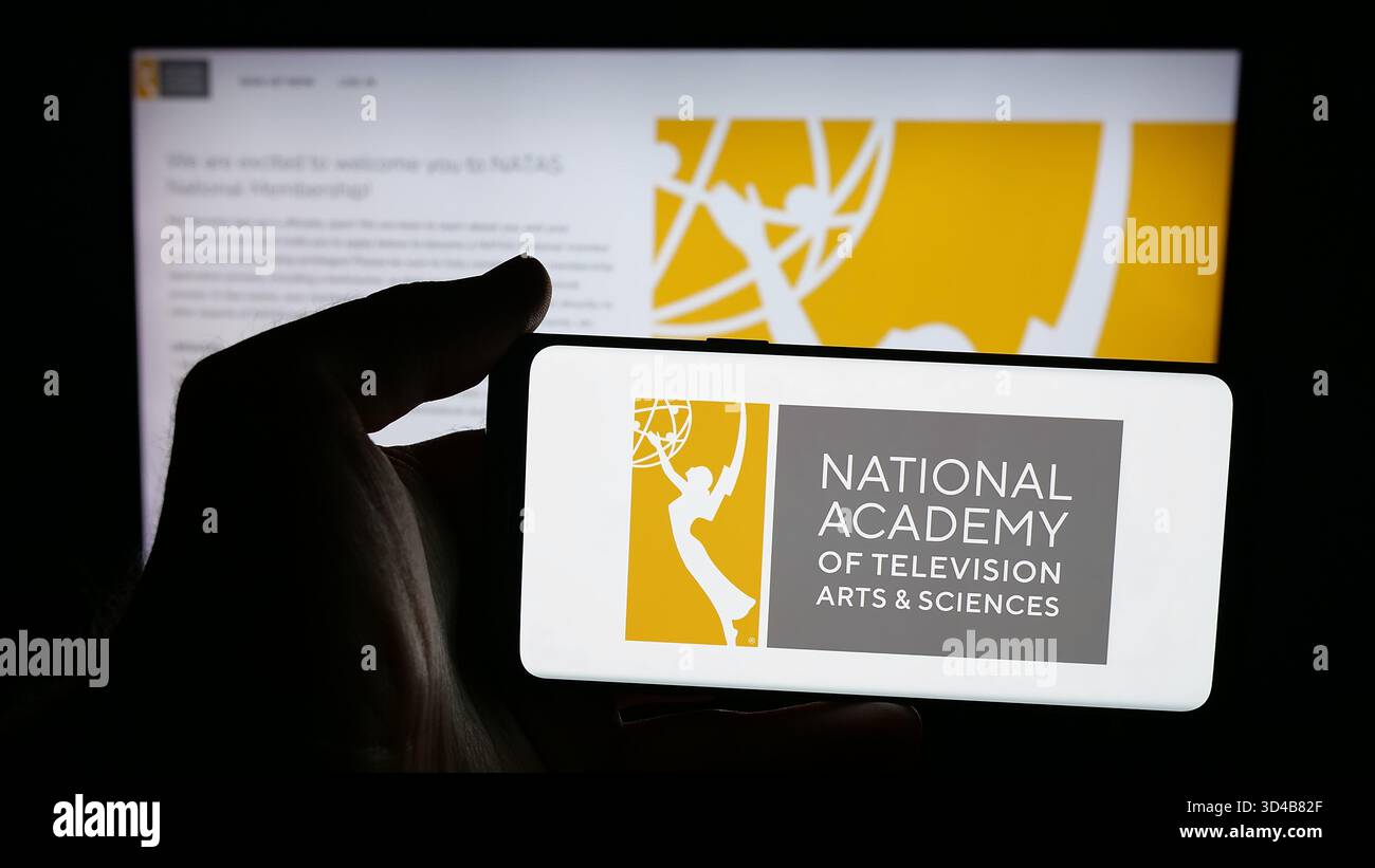 Stuttgart, Deutschland - 10-31-2025: Person, die ein Mobiltelefon mit dem Logo des US-Fernsehpreises Emmys (Emmys) auf dem Bildschirm vor der Webseite hält. Stockfoto