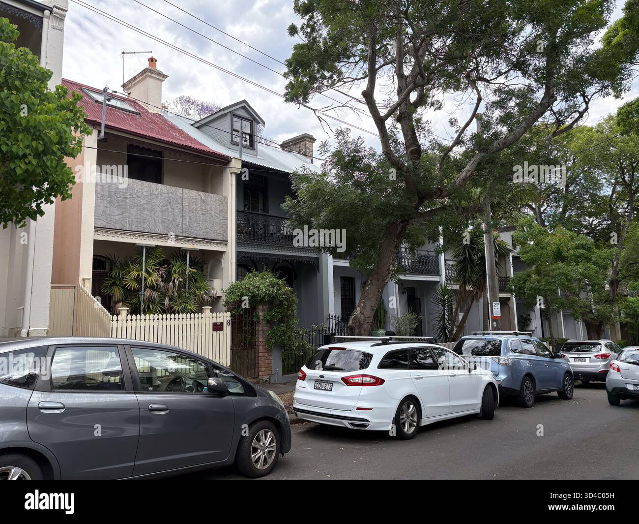 Eine Reihe historischer Reihenhäuser säumen eine Wohnstraße in Sydney, Australien, mit geparkten Autos entlang der Bordsteinkante. Die Architektur verfügt über Balkone Stockfoto
