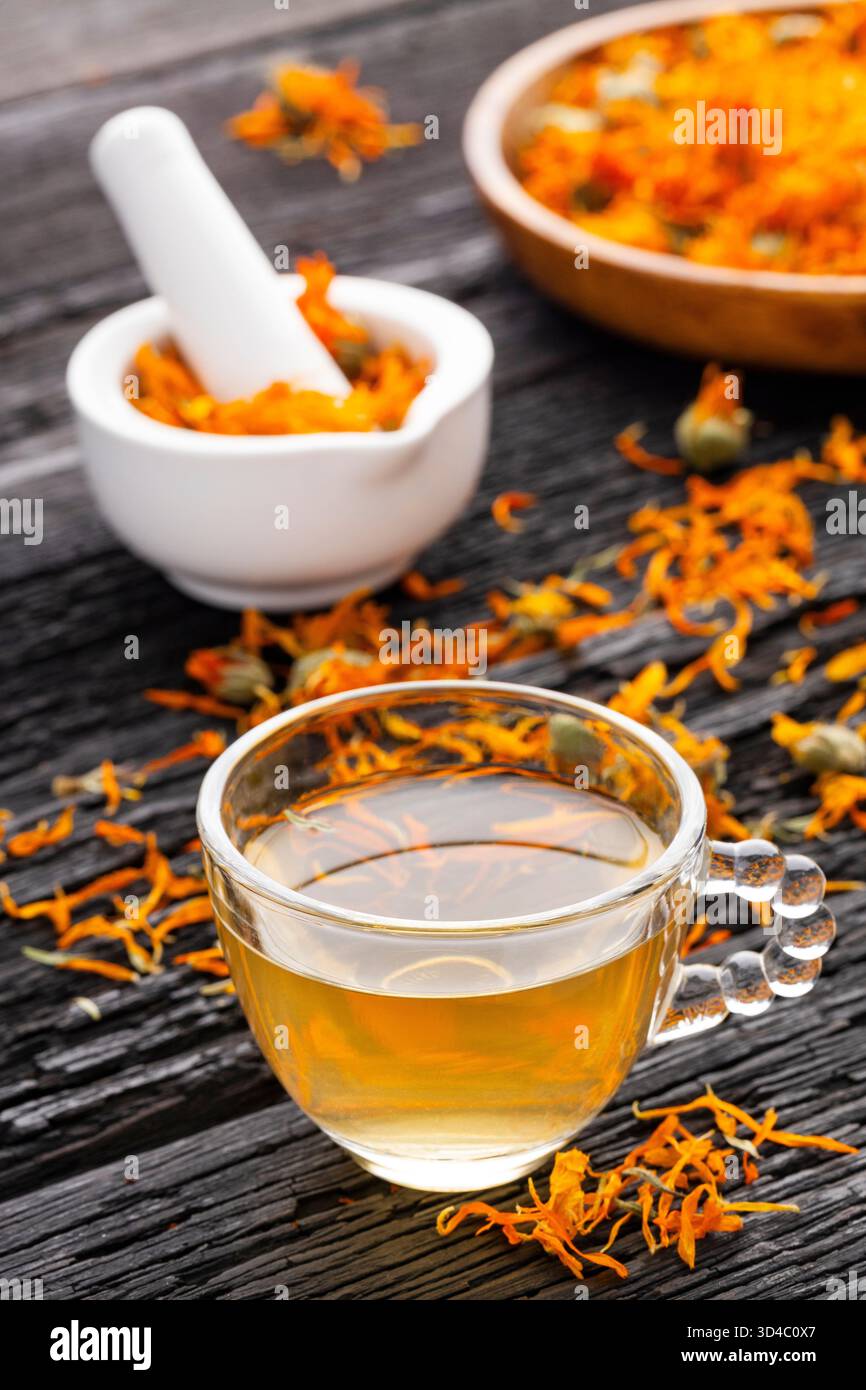 Tasse Calendula Tee, begleitet von getrockneten Blütenblättern und einem weißen Mörtel mit Calendula Blumen - Calendula officinalis Stockfoto
