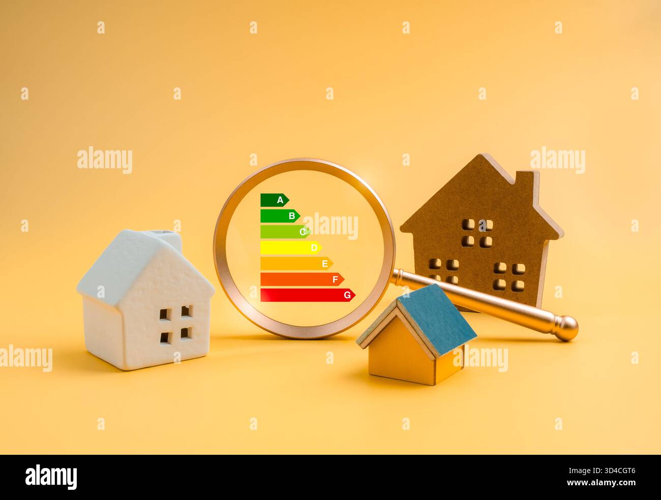 Energieeffizienzkonzept mit farbenfroher Skala A bis G, fokussiert in Lupenlinse und verschiedenen Hausmodellen, symbolisiert den Energieeinfluss im Haus Stockfoto