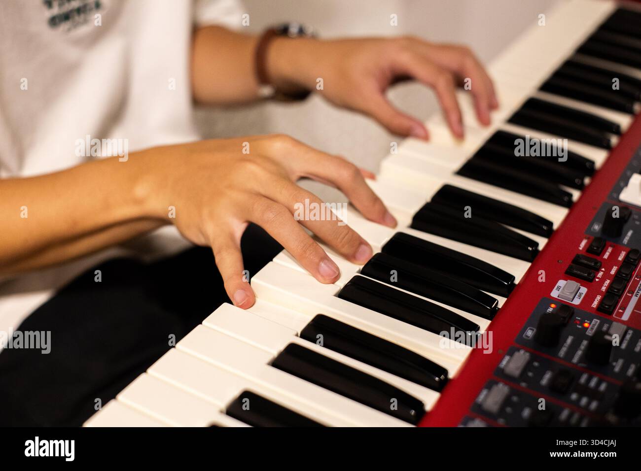 Nahaufnahme eines Musikers, der drinnen eine rote elektronische Tastatur spielt und fokussierte Handbewegungen über die Klaviertasten zeigt Stockfoto