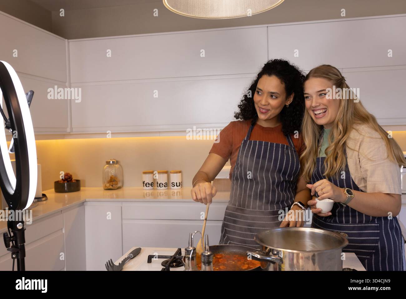 Rührsoße verschiedene weibliche Freunde kochen auf Gasherd in moderner Küche, mit Ringlicht Stockfoto