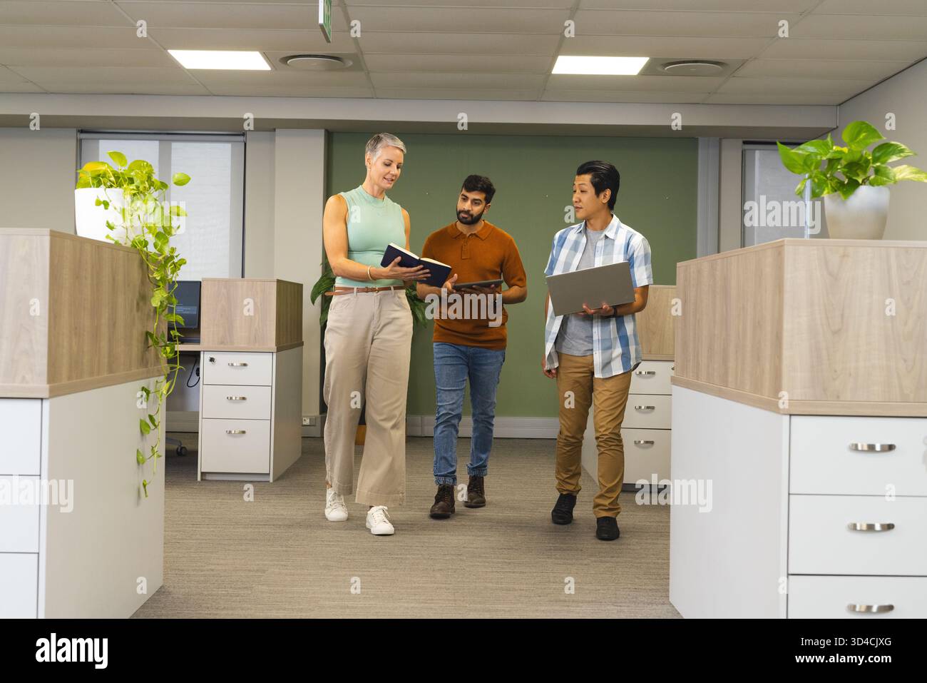 Verschiedene Kollegen mit Notebook-Tablet-Laptop im Bürogang und unter Deckenleuchten unterwegs sind Stockfoto