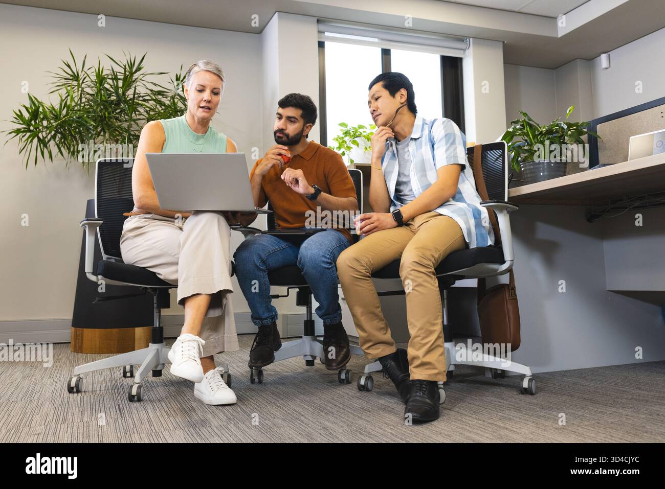 Zusammenarbeit mit verschiedenen Kollegen, die in modernen Büroräumen mit Topfpflanzen um ein Notebook sitzen Stockfoto