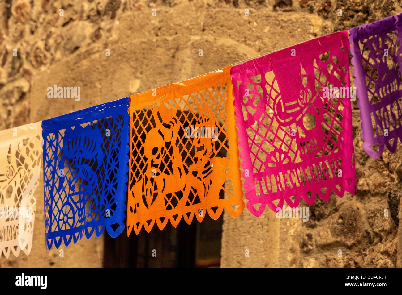 Eine bunte Schnur aus Papierlaternen hängt an einer Wand. Die Laternen sind in verschiedenen Farben und Formen. Mexikanischer Tag der Toten Tradition, Opfer, Foo Stockfoto