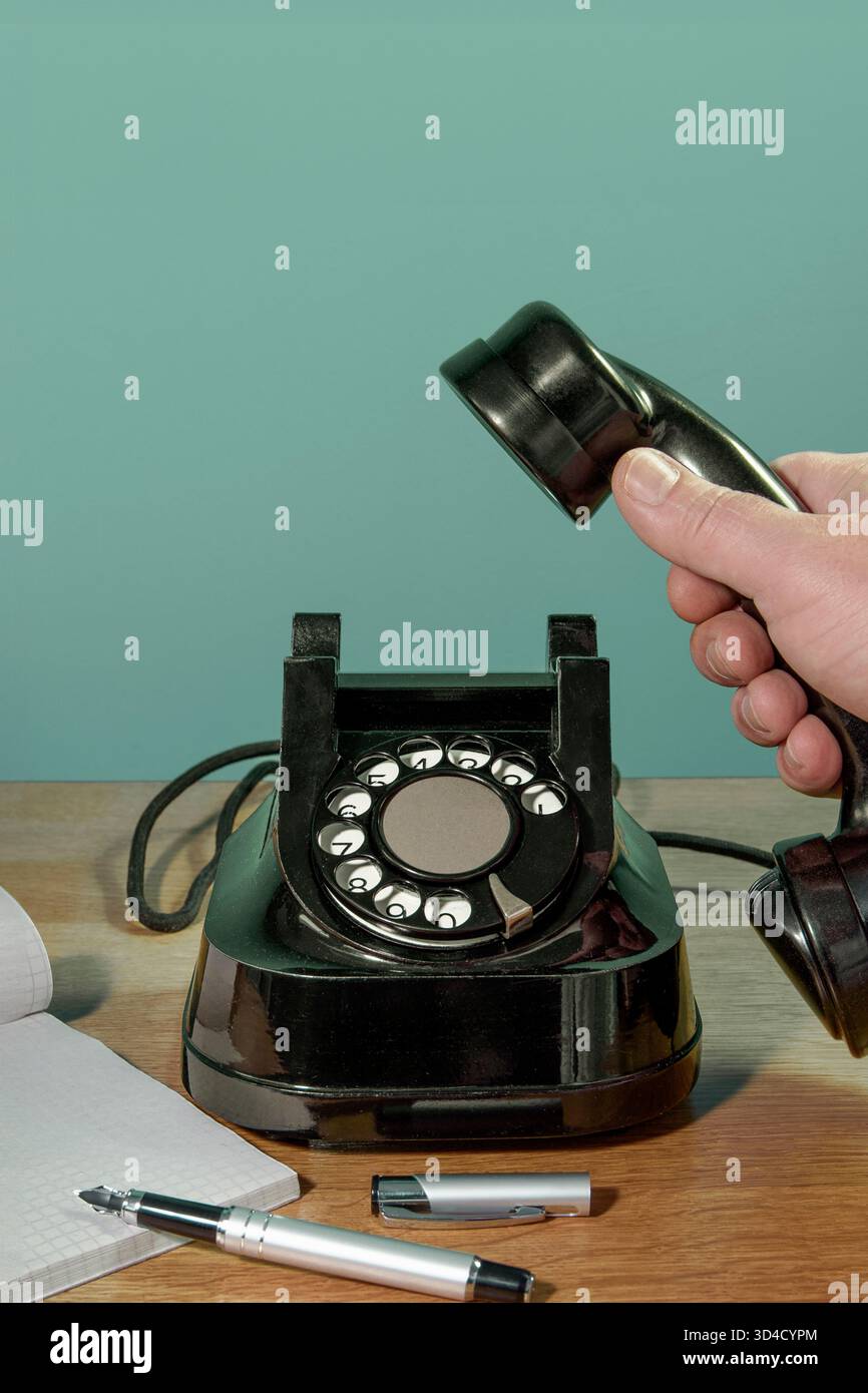 Retro-Telefon, Hand mit Notebook und Stift den Telefonhörer auf dem Schreibtisch abheben. Vertikales Banner auf Grün Stockfoto