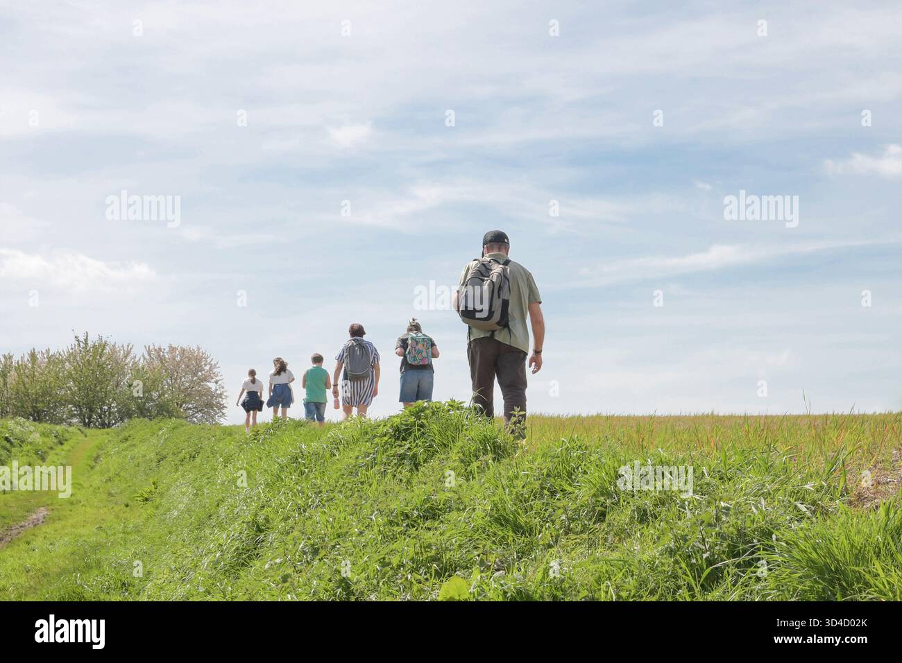 Eine Gruppe von Menschen läuft auf einem Feld mit einem Mann in der Mitte. Der Mann trägt einen Rucksack und hat einen Bart Stockfoto