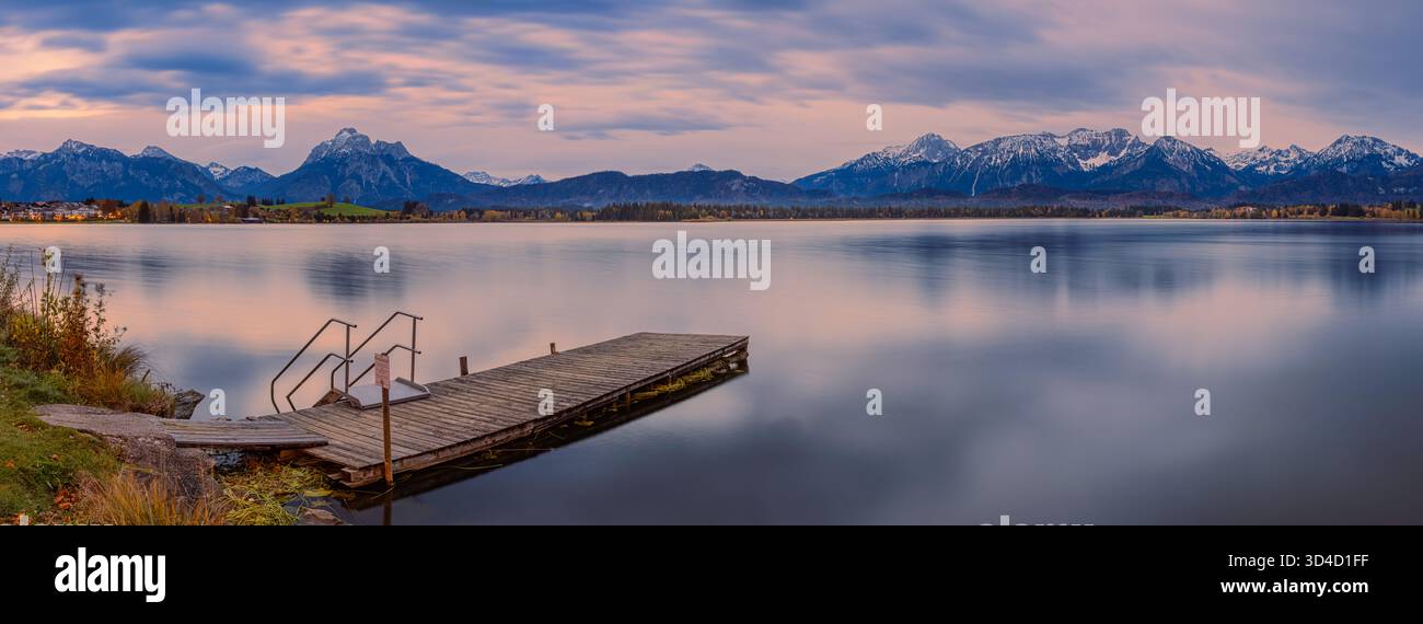 Großer Panoramablick auf den Sonnenaufgang über Hopfensee in Hopfen am See, Bayern, Deutschland, aufgenommen in einem filmischen 65:24 XPan-Format. Das stille Wasser des Sees Stockfoto