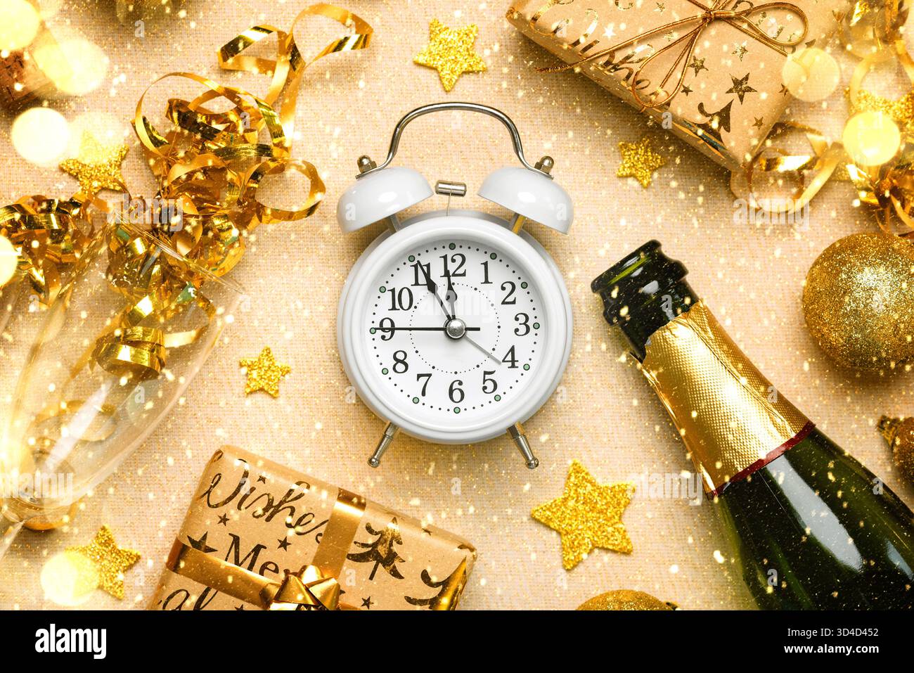 Blick von oben auf den weißen Wecker mit einer Flasche Champagner, Kristallgläsern, goldenen weihnachtskugeln und Weihnachtsgeschenken auf einer goldenen Glitzertischdecke Stockfoto