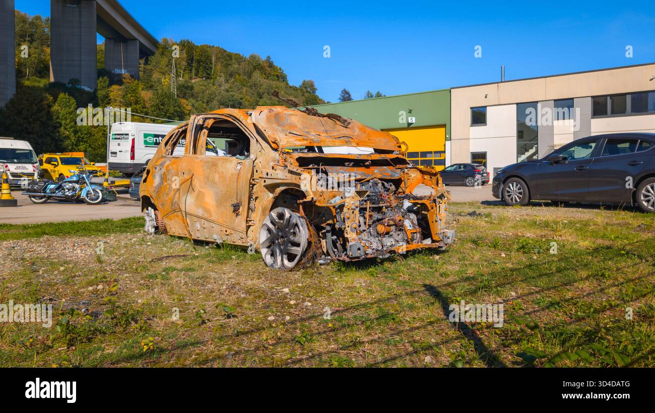 Verbranntes Auto bleibt nach einem Brandunfall auf einem Parkplatz in einem Industriegebiet mit anderen Fahrzeugen im Hintergrund. Stockfoto