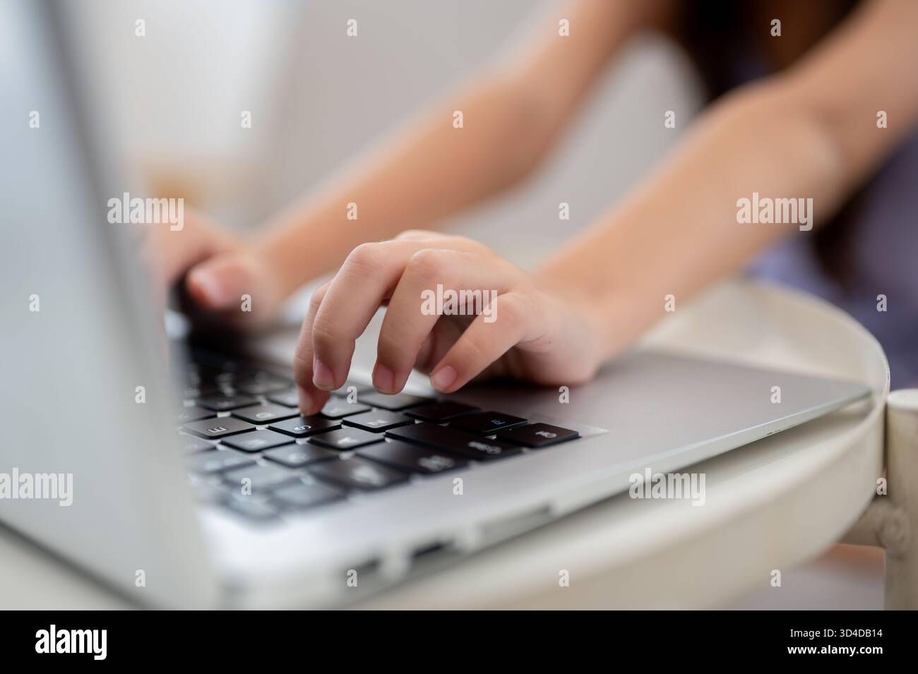 Nahaufnahme eines Paares Kinderhände, die auf einem weißen Tisch auf einem Laptop tippen, während sie auf dem Sofa sitzen. Daten durchsuchen oder Hausaufgaben machen. Stockfoto