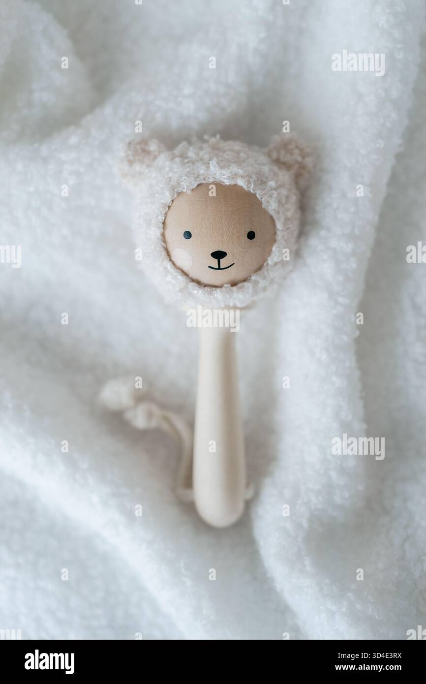 Minimales Studiobild einer hölzernen Babyrassel auf einer weißen texturierten Decke, saubere, weiche Ästhetik für Produktangebote von Neugeborenen und sanften Lebensstil Stockfoto