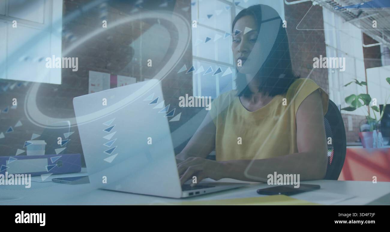 Reife Frau mit silbernem Laptop im Büro mit Grafik-Overlay, Senfoberteil Stockfoto