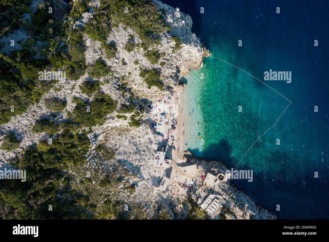 Blick aus der Vogelperspektive auf türkisfarbenes Wasser, zerklüftete Klippen und einen sonnendurchfluteten Strand voller Leben, Brsec, Istrien, Kroatien. Stockfoto