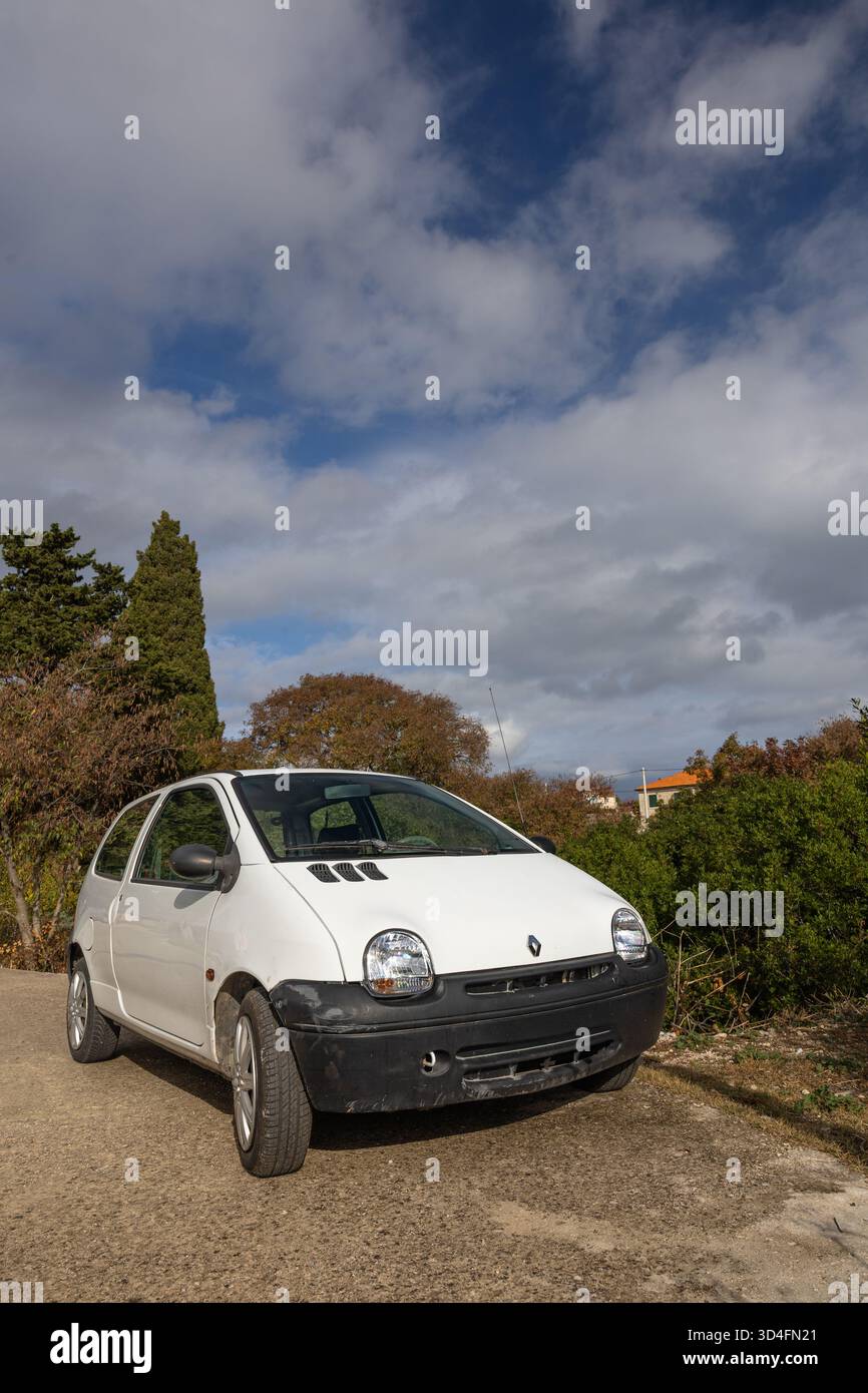 GROHOTE, KROATIEN, 10.23.2025: Ein kleiner weißer Renault Fließheck, der auf einer Schotterstraße geparkt ist und von Herbstbäumen umgeben ist. Helles Sonnenlicht und eine ruhige, ländliche Umgebung Stockfoto