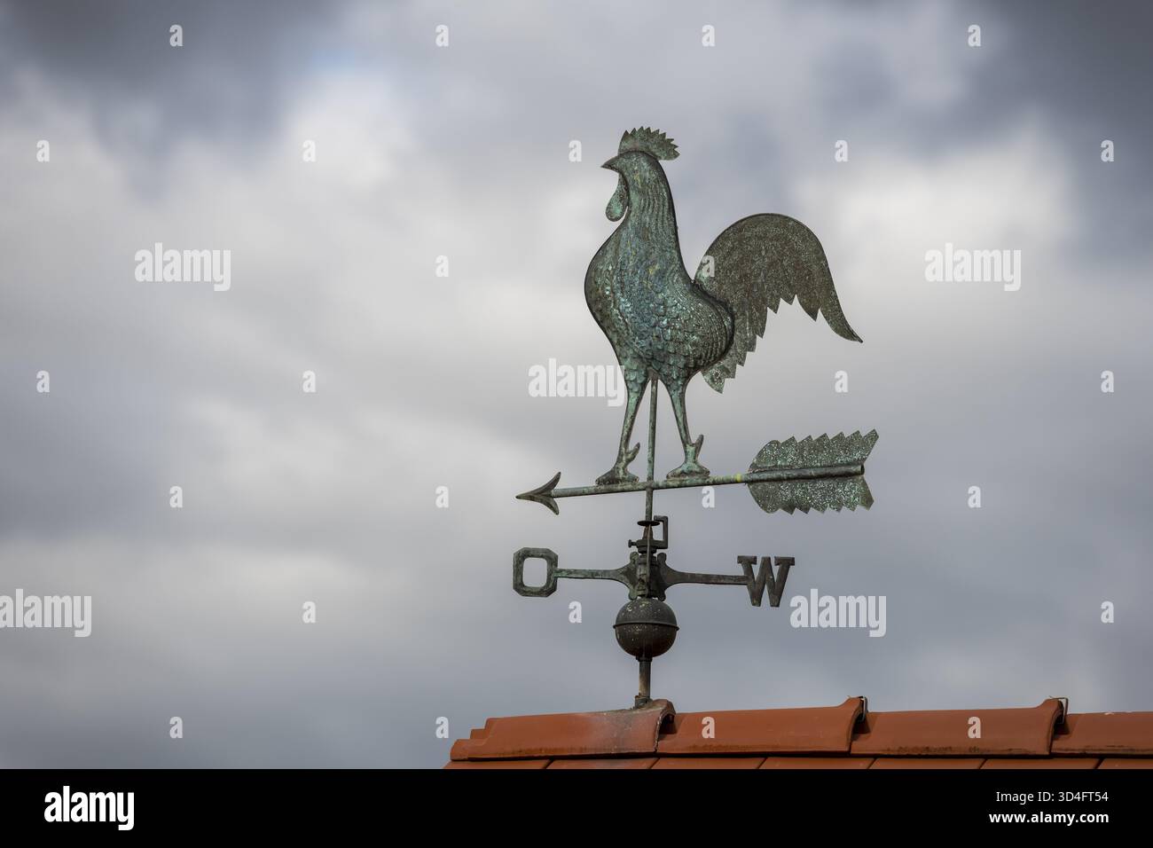 Hahn Wetterfahne auf einem gekachelten Dach vor dunklem bewölktem Himmel, Baden-Württemberg, Deutschland Stockfoto