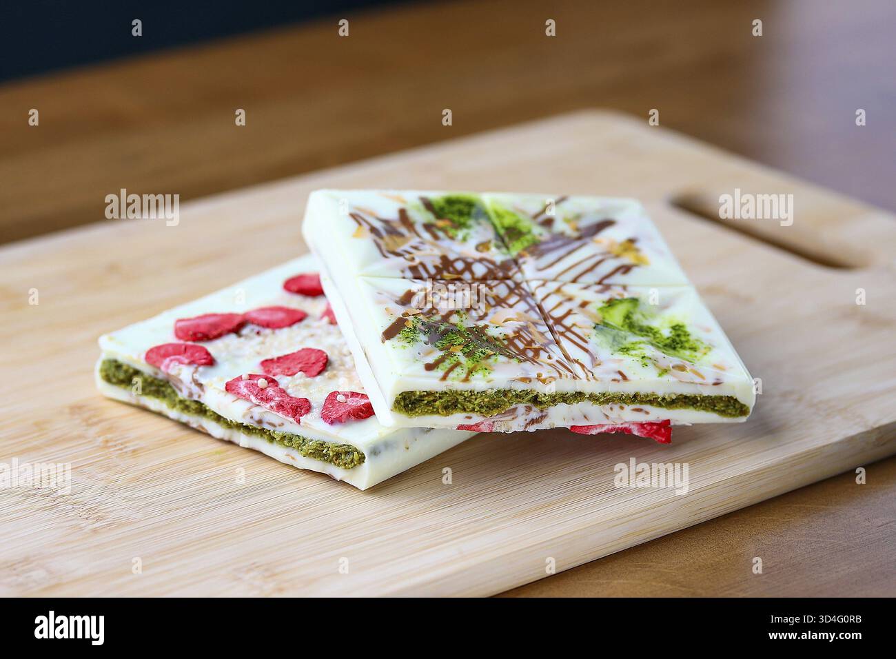 Speisen, weiße Gourmet-Schokoladentafeln mit Matcha-Schicht gefriergetrocknete Erdbeeren und Nüsse auf einem Bambus-Schneidebrett Stockfoto