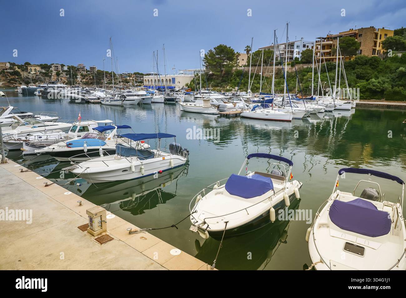 Der Hafen von Porto Cristo auf Mallorca bietet eine ruhige Szene mit Booten, die sanft vor der Kulisse von Küstengebäuden und üppigem Grün ankern Stockfoto