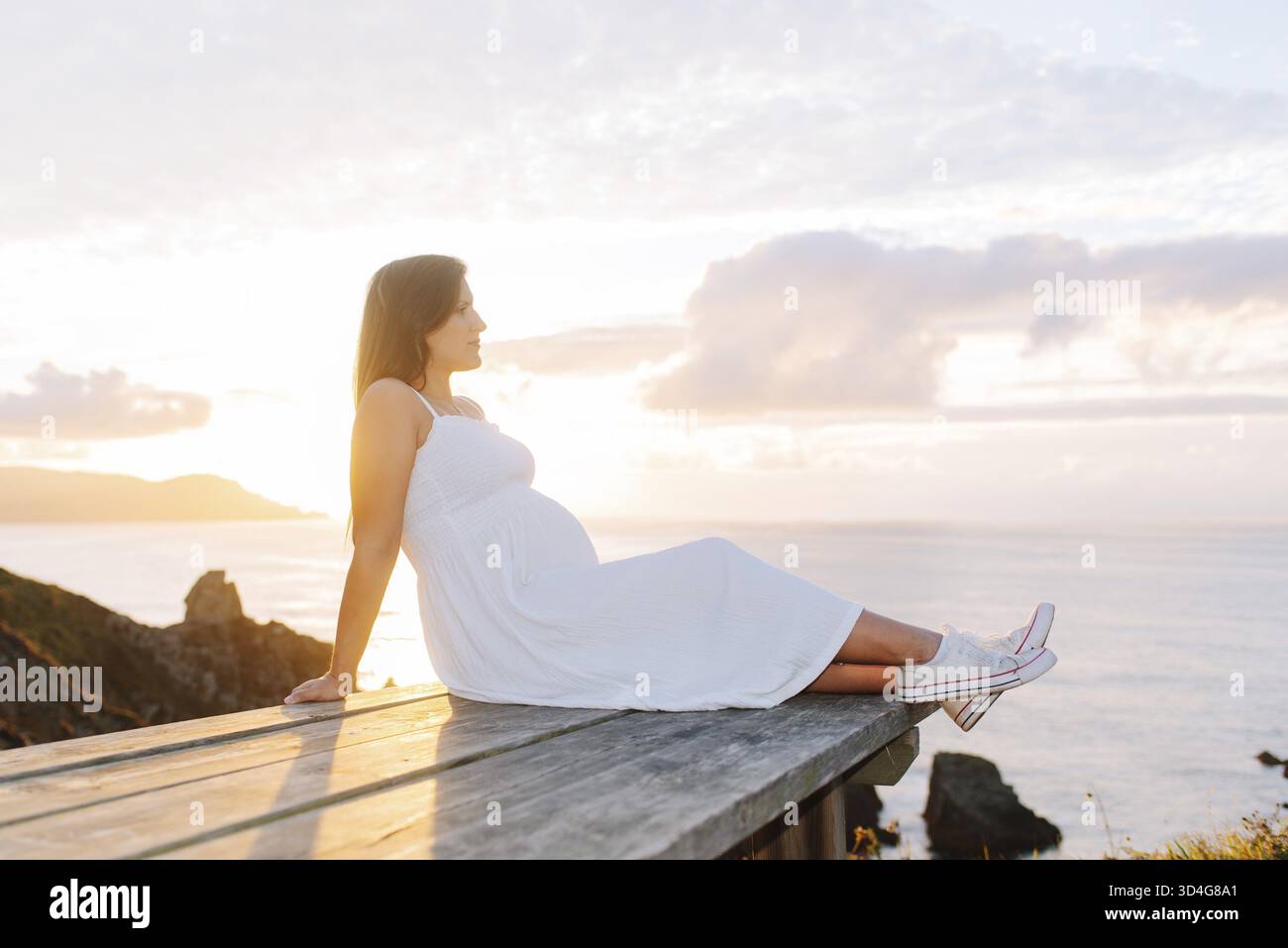 Porträt einer schwangeren Frau gegen eine ozeanische Landschaft bei Sonnenuntergang in Galicien, Spanien Stockfoto