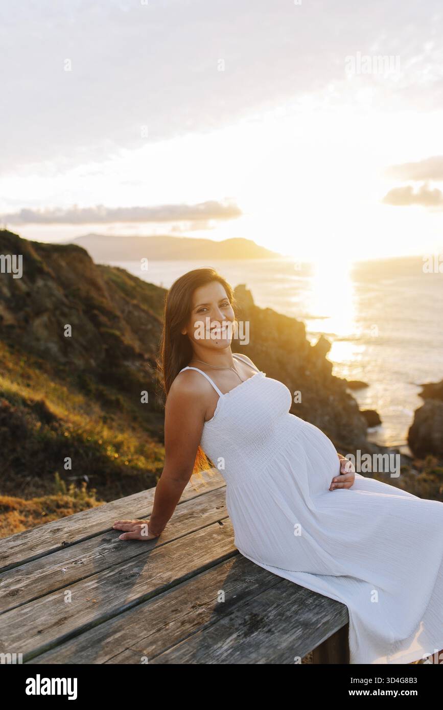 Porträt einer schwangeren Frau gegen eine ozeanische Landschaft bei Sonnenuntergang in Galicien, Spanien Stockfoto