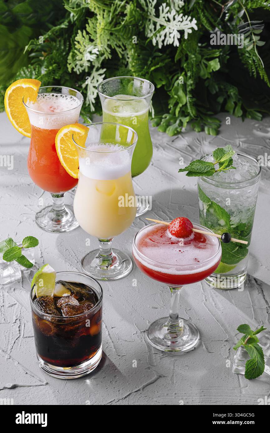 Essen, Auswahl an bunten Cocktails garniert mit Früchten auf einem strukturierten weißen Tisch Stockfoto