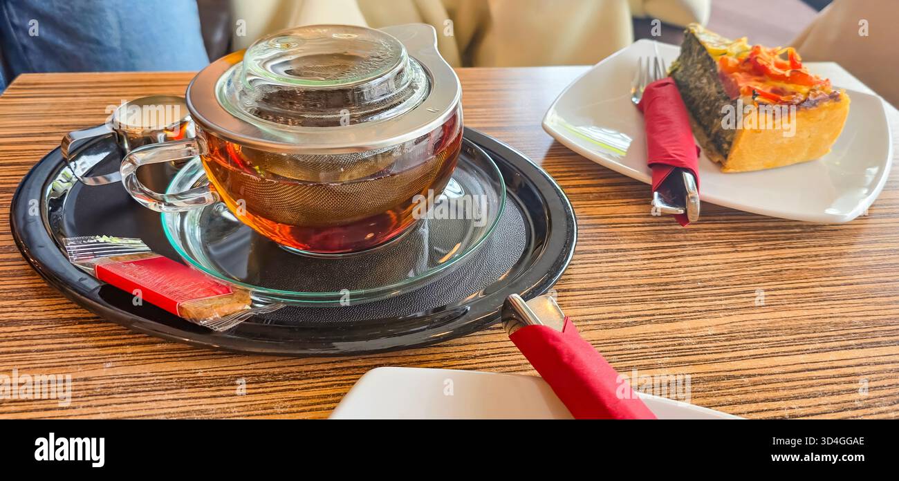 Eine mit gebrühtem Tee gefüllte Glaskanne steht auf einem Holztisch neben einem Stück Dessert und schafft so eine gemütliche Atmosphäre. - Smartphone-aufgenommenes Stockfoto