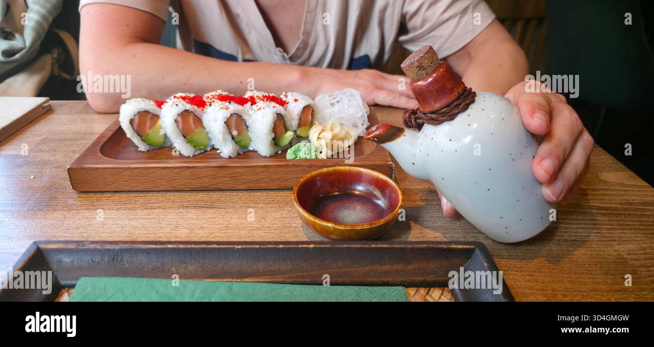 Die Sushi-Platte bietet lebendige Brötchen, Wasabi und Dip-Sauce auf einem rustikalen Holztisch, was ein einladendes kulinarisches Erlebnis schafft. - Smartphone-aufgenommenes Stockfoto
