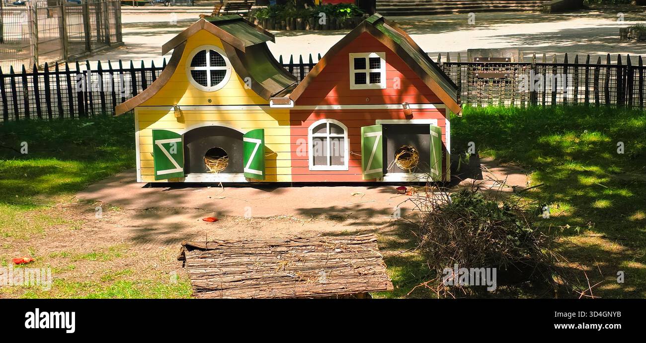 Farbenfrohe Tierhäuser befinden sich in einem sonnigen Park, umgeben von grünen Gras und Bäumen, die eine verspielte und einladende Atmosphäre schaffen. - Smartphone-aufgenommenes Stockfoto