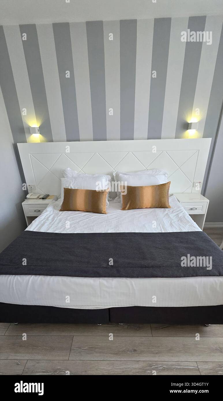 . Modernes Hotelzimmer mit stilvollem Dekor, eleganter Beleuchtung und einem komfortablen Bett mit dekorativen Kissen für eine gemütliche Atmosphäre - Smartphone-aufgenommenes Stockfoto