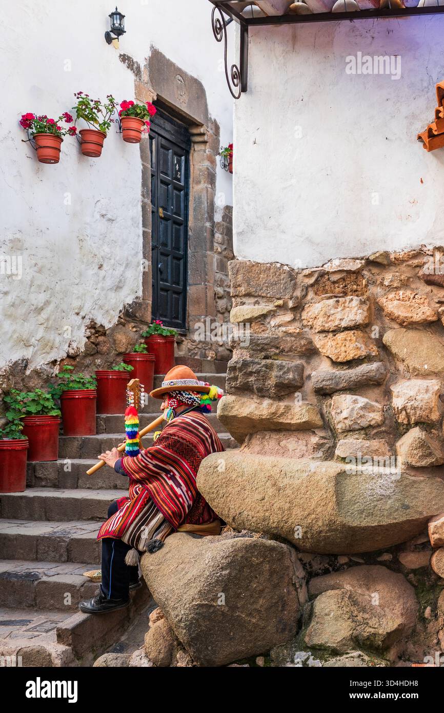 Lokaler Musiker in traditioneller Kleidung, der auf Steintreppen sitzt, die mit Blumentöpfen dekoriert sind, im Viertel San Blas, Cusco, Peru. Stockfoto