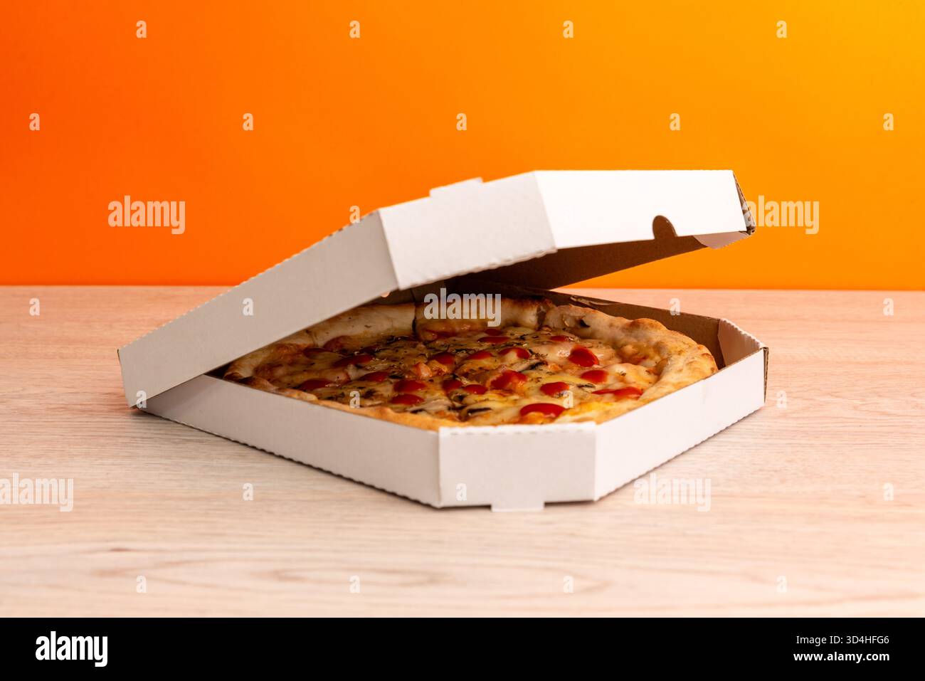 Pizza in halb geschlossener Box auf Holztisch mit orangem Hintergrund, symbolisiert frische Lieferung, Fast Food und moderne Restaurantverpackung Stockfoto