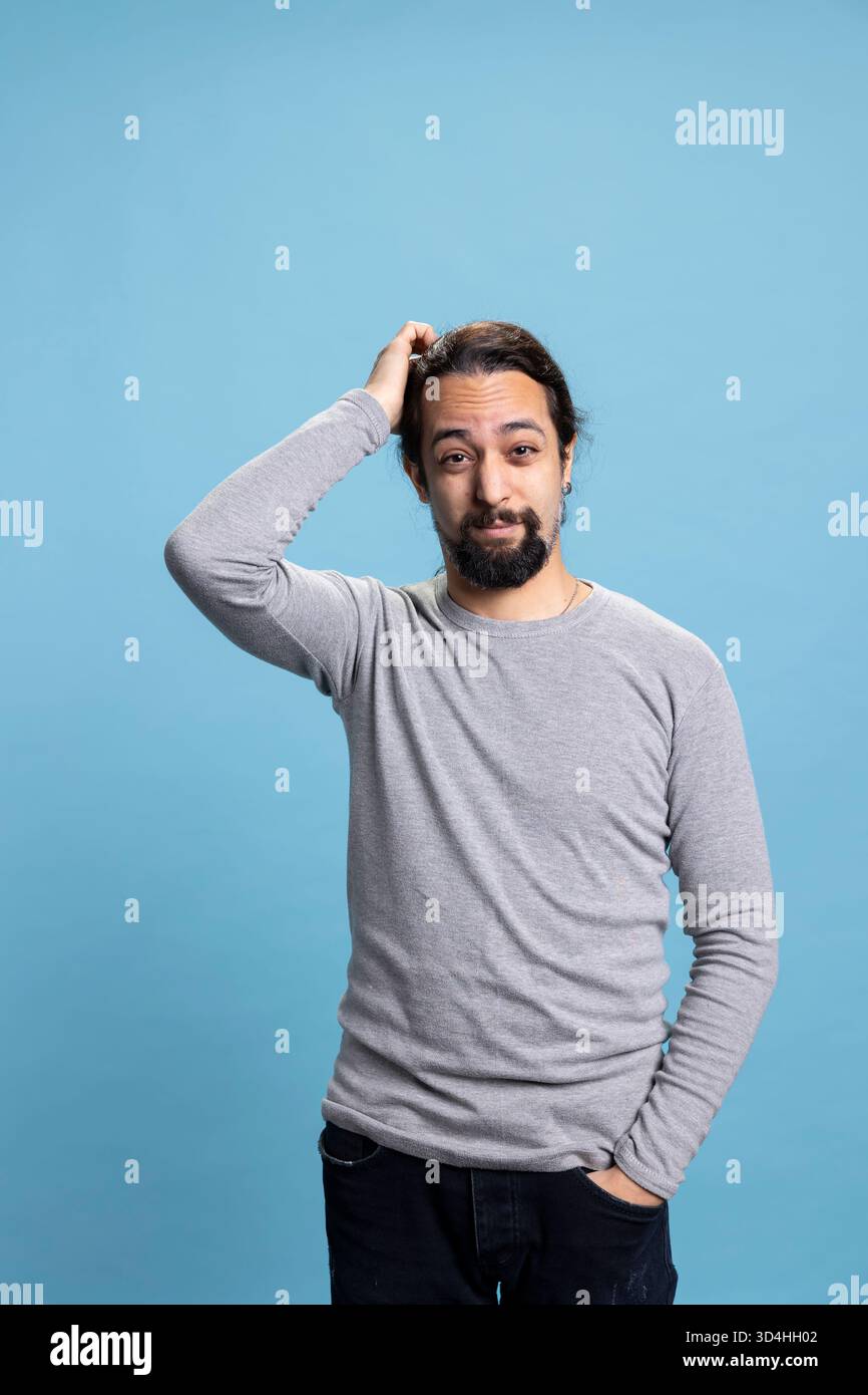 Unsichere Person aus dem Nahen Osten, die sich unsicher und verwirrt vor blauem Hintergrund fühlt, nachdenkt und neugierig im Studio ist. Junge Erwachsene, die nachdenklich und nachdenklich handeln, Entscheidungen treffen. Stockfoto