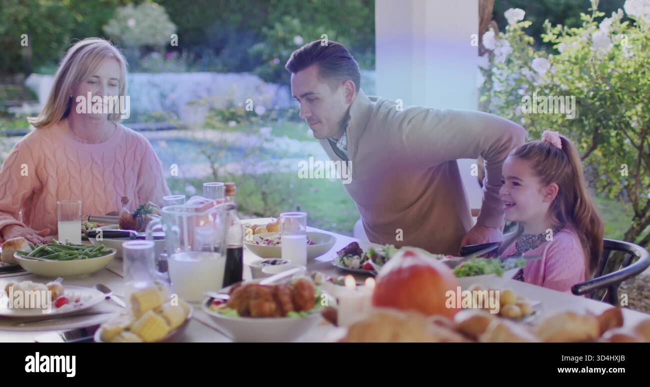 Familie, die auf der Veranda am Tisch sitzt, rosafarbene Pullover-Frau, Mann geneigt, gebratenes Huhn Stockfoto