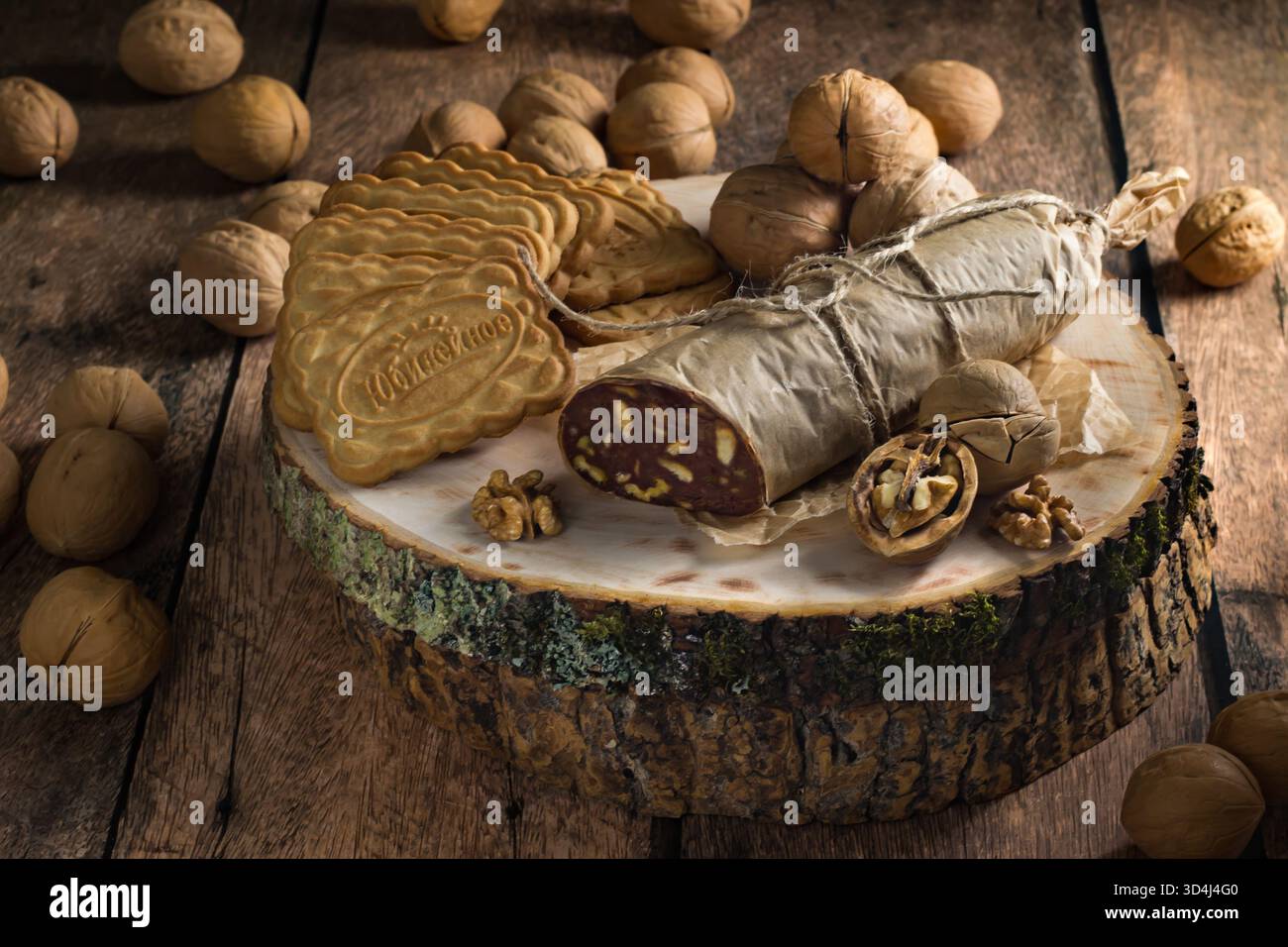 Gemischte Nüsse und süße Kekse sind auf einer Holzplatte angeordnet und zeigen ein in Blätter gehülltes Dessert in Form von Baumstämmen. Dieses schöne Display sorgt für einen warmen, Stockfoto